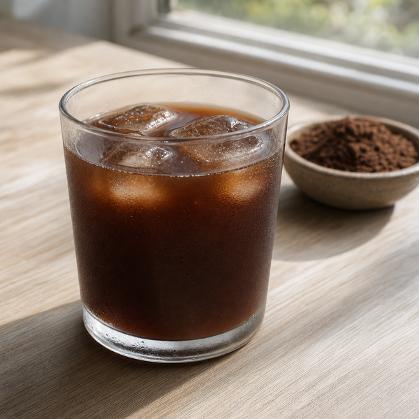 Glass of chilled brewed cacao with ice beside ground brewing cacao on a sunlit wooden windowsill